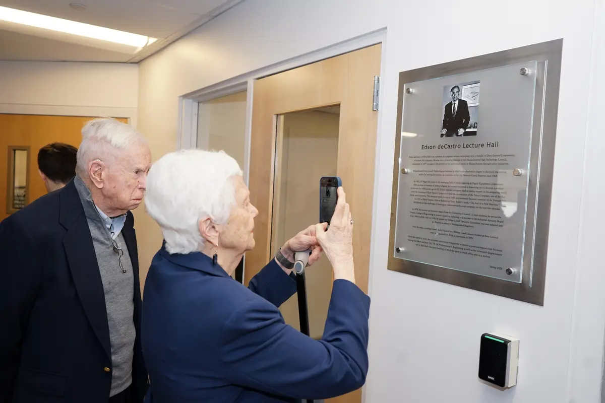 A woman uses her phone to take a picture of a wall-mounted plaque while a man looks on.