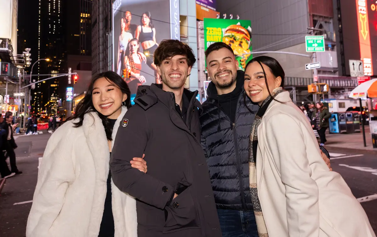 Four young men and women pose for a photo at night in New York's Times Square.