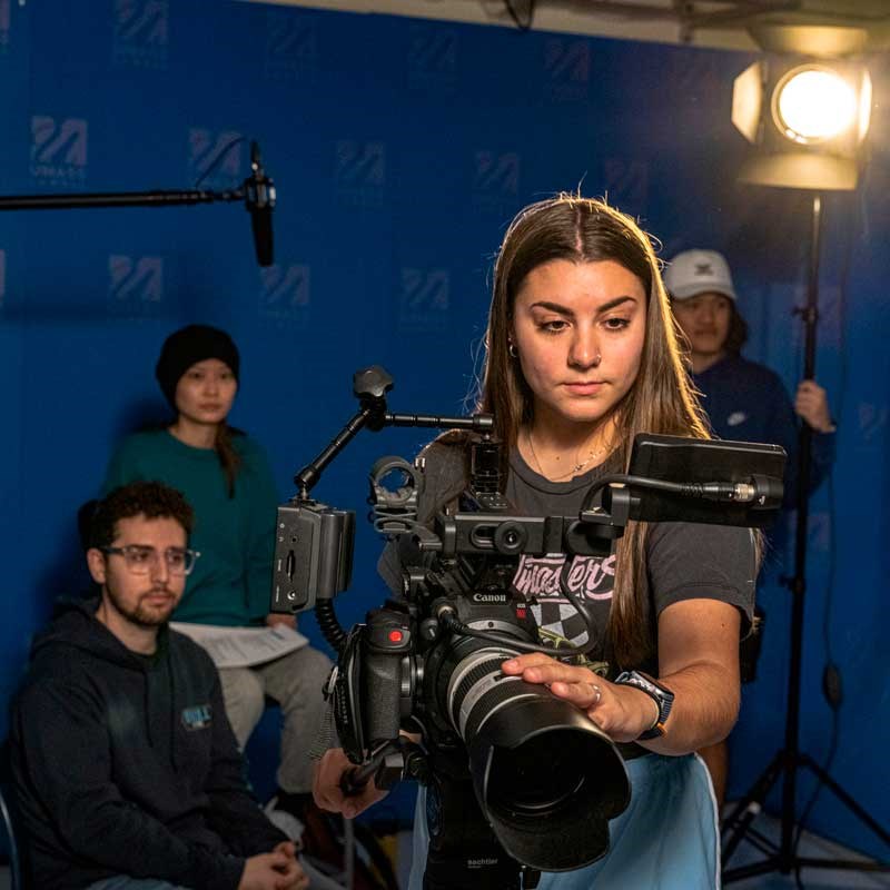 Digital media student focuses a video camera in a UMass Lowell studio
