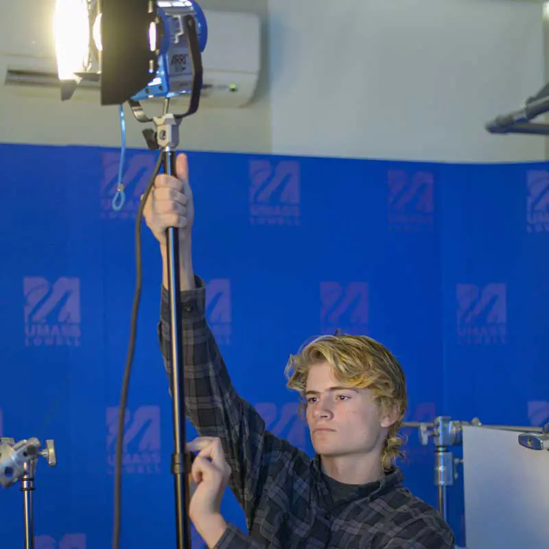 Digital media student holds a light in a UMass Lowell filming studio