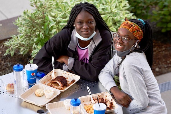 Two students pose for a photo while eating dinner outside