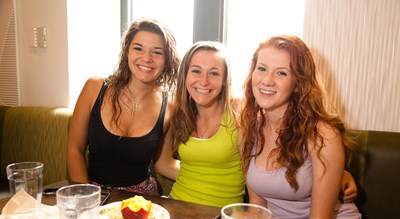 Three female college students posing for a picture while eating at a dining hall. UMass Lowell Dining Services provides three meal plan options for residential students. These meal plans give students choices, flexibility and the River Hawk dollars they crave. All of the new plans include eight guest meals each semester-allowing students to bring their friends and family into the dining halls when they visit!