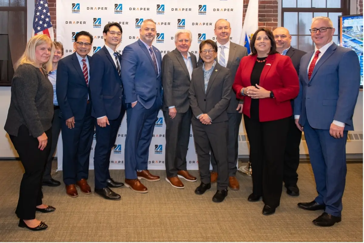 11 men and women wearing suits stand in front of a Draper banner, including Marty Meehan, Julie Chen and Lt. Gov. Kim Driscoll