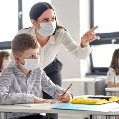 Masked teacher helps masked student in classroom