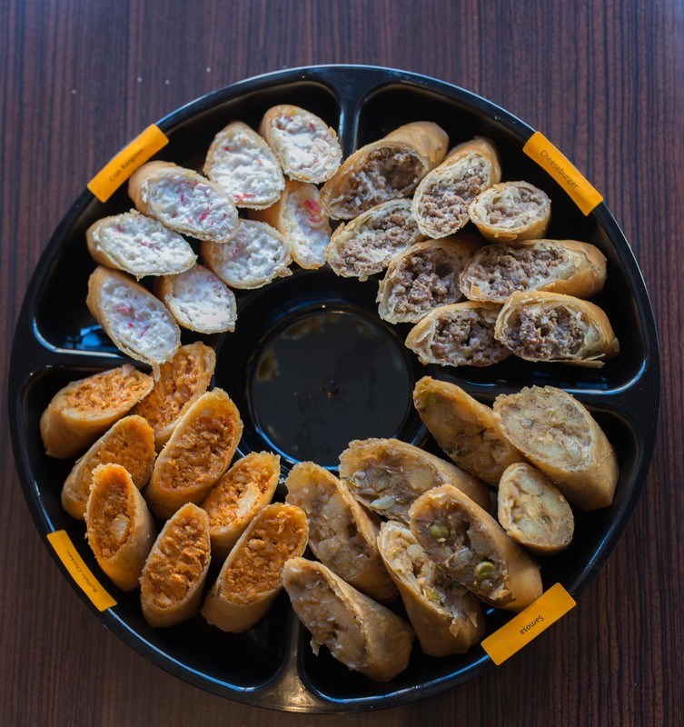 A circular tray displaying crab rangoon egg rolls, cheeseburger egg rolls, samosa egg rolls and buffalo chicken egg rolls