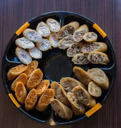 A circular tray displaying crab rangoon egg rolls, cheeseburger egg rolls, samosa egg rolls and buffalo chicken egg rolls