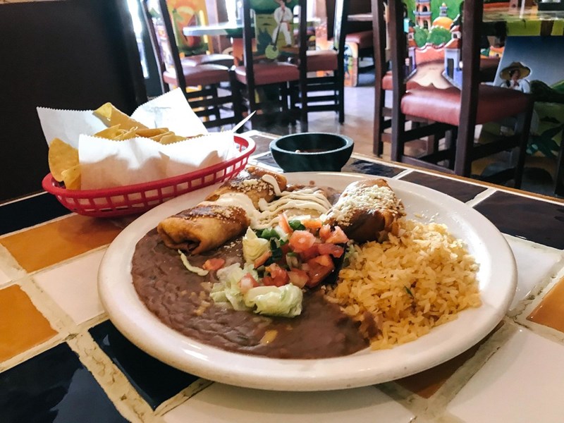 a Mexican entree with rice, beans, tortilla chips and salsa sit atop a colorful tiled table