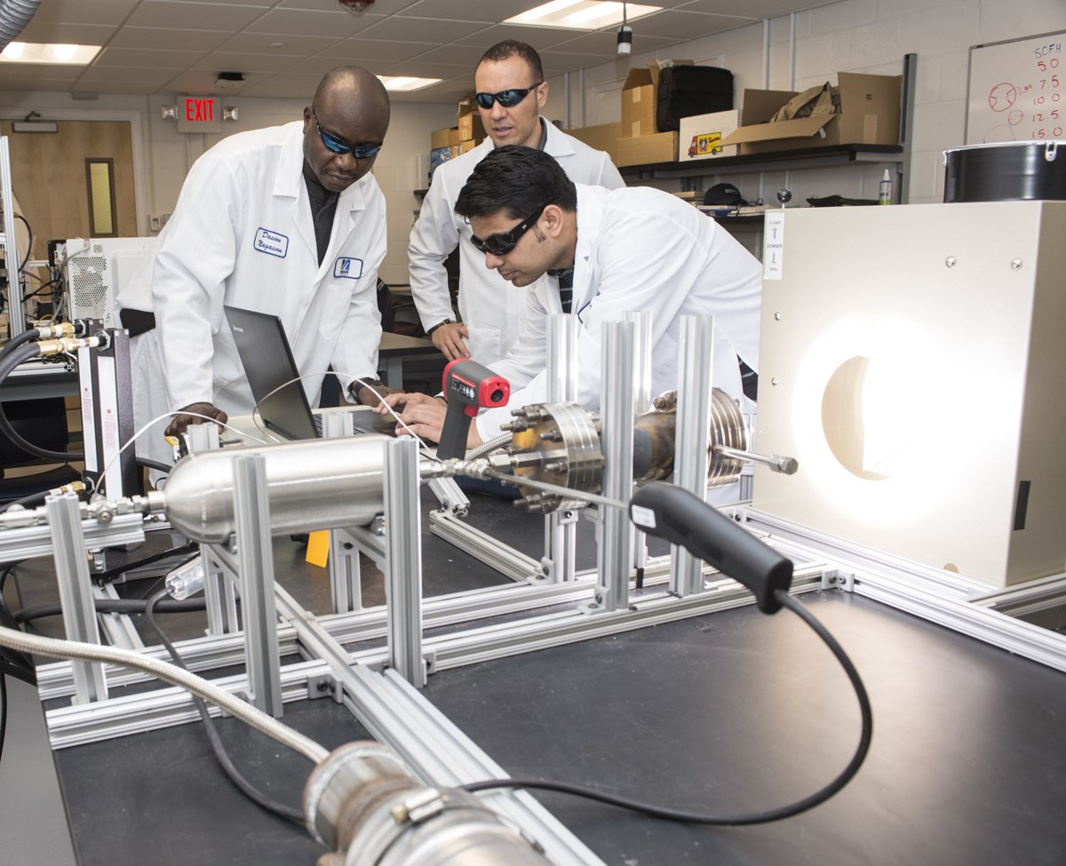 Three men in white lab coats work in lab