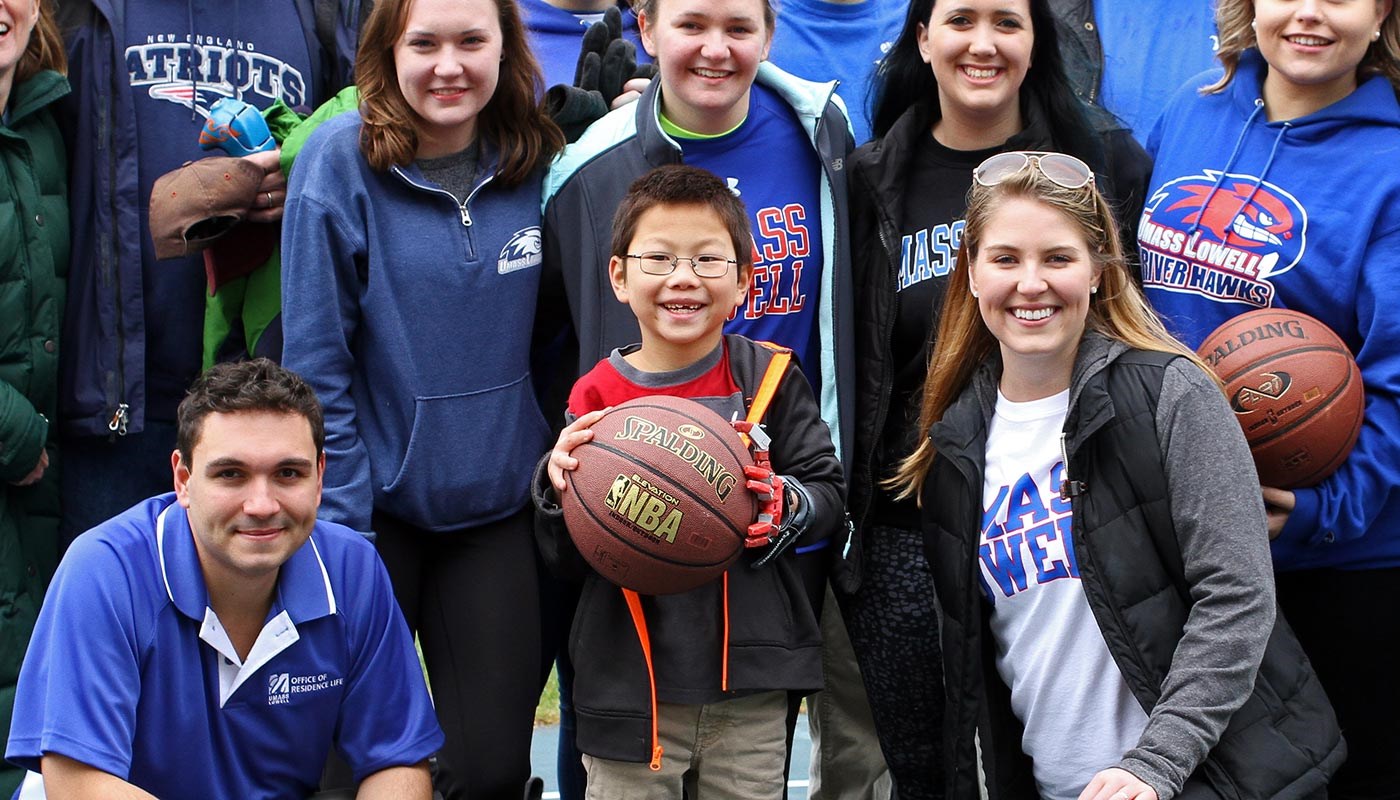 Child with prosthetic hand holding a basketball surrounded by students