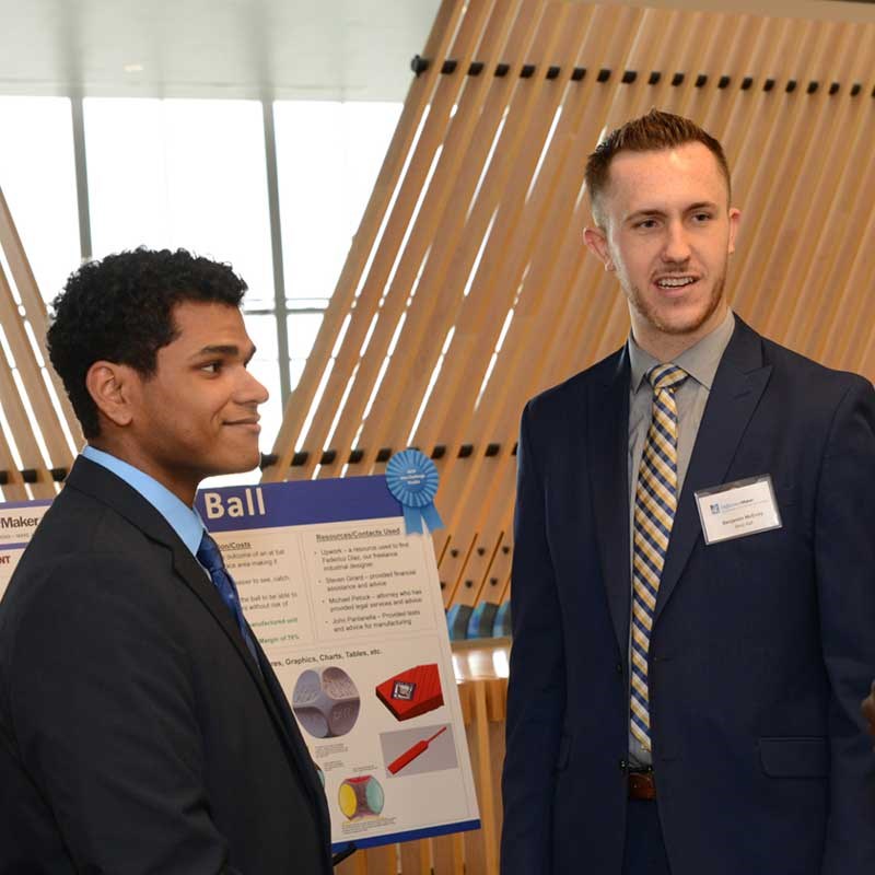 Edward Morante (left) stands with Benjamin McEvoy in front of their poster at a DifferenceMaker event, talking to a student