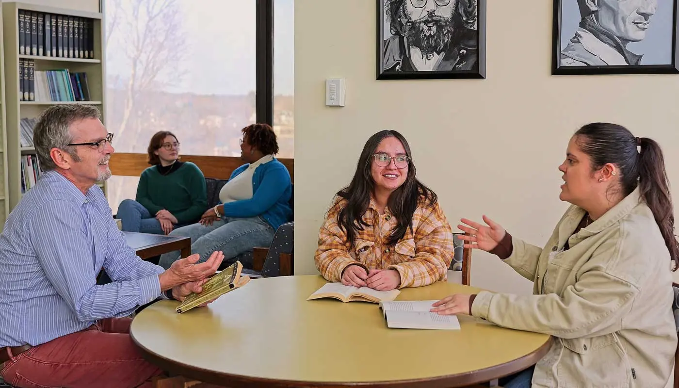 Two students and a professor discuss a book in an English classroom at UMass Lowell.