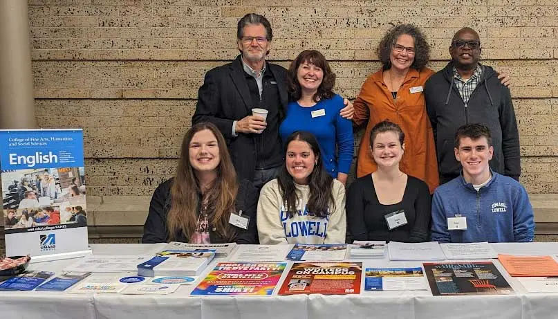 UMass Lowell English students and professors gather at a table displaying department information.