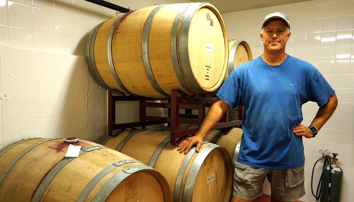 Eric Preusse stands in front of barrels of wine at his vineyard, Broken Creek
