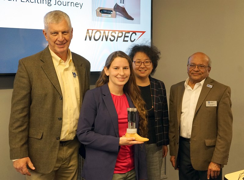 Erin Keaney holding a prosethic with Jack Wilson, UMass president emeritus and UMass Lowell distinguished professor of higher education, emerging technologies and innovation; and Manning School of Business faculty members Yi Yang and Ashwin Mehta.