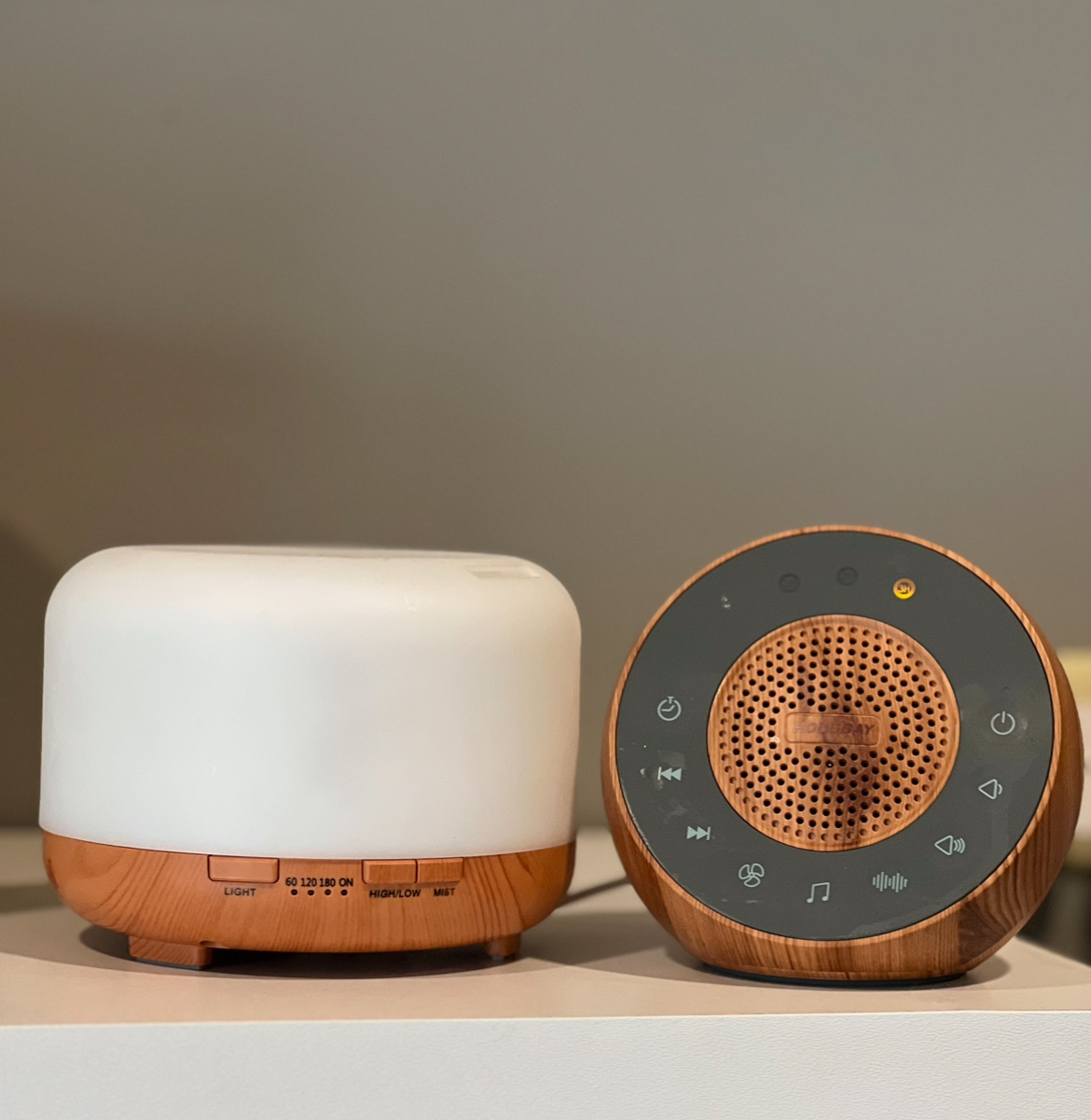White essential oil diffuser with a wooden bottom, wooden circular sound machine with a grey interior housing buttons for different sounds.