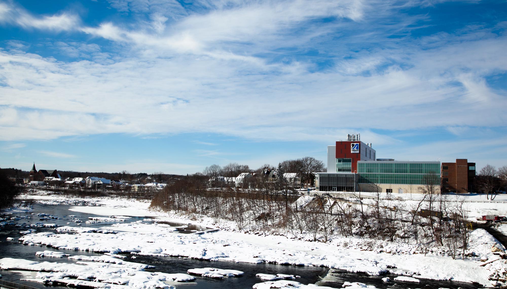 View of the Saab Emerging Technology & Innovation Center across the Merrimack River on a snowy day.