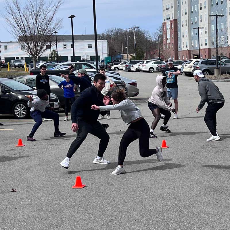 A group of students completing a Exercise Science training in a parking lot located outside of a UMass Lowell academic building. 