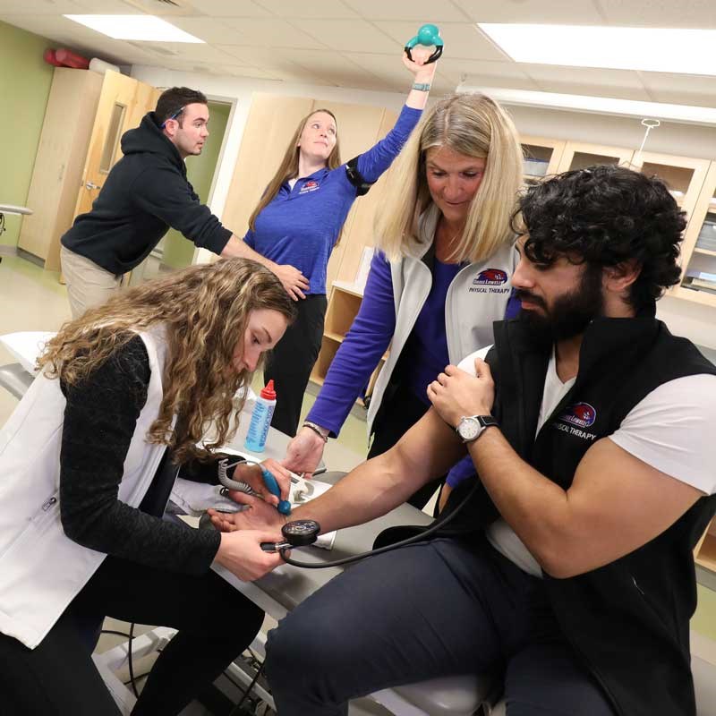 A professor watches as an exercise students reads the pulse of another student in a UMass Lowell lab