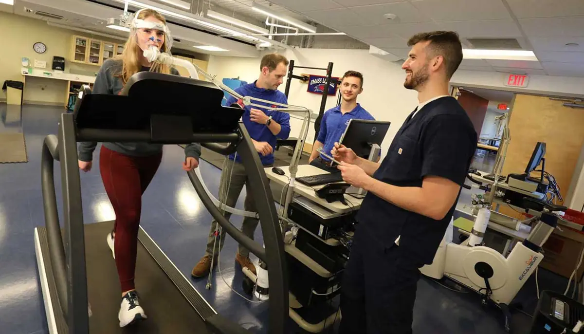 A student walks on a treadmill while wearing testing equipment on her mouth as another student observes in a UMass Lowell exercise science lab