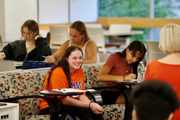a girl smiles while other students around write in notebooks