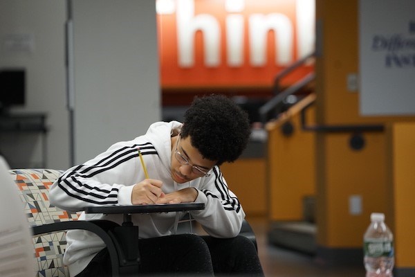 A student in glasses is hunched over a desk while he writes 