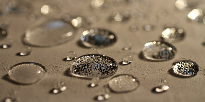 Closeup picture of water droplets on a golden colored waterproof fabric