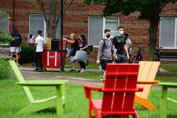 Students move on to campus as green, red and yellow Adirondack chairs sit in the foreground