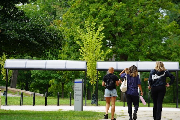 Three students walk on a path toward covered bicycle racks