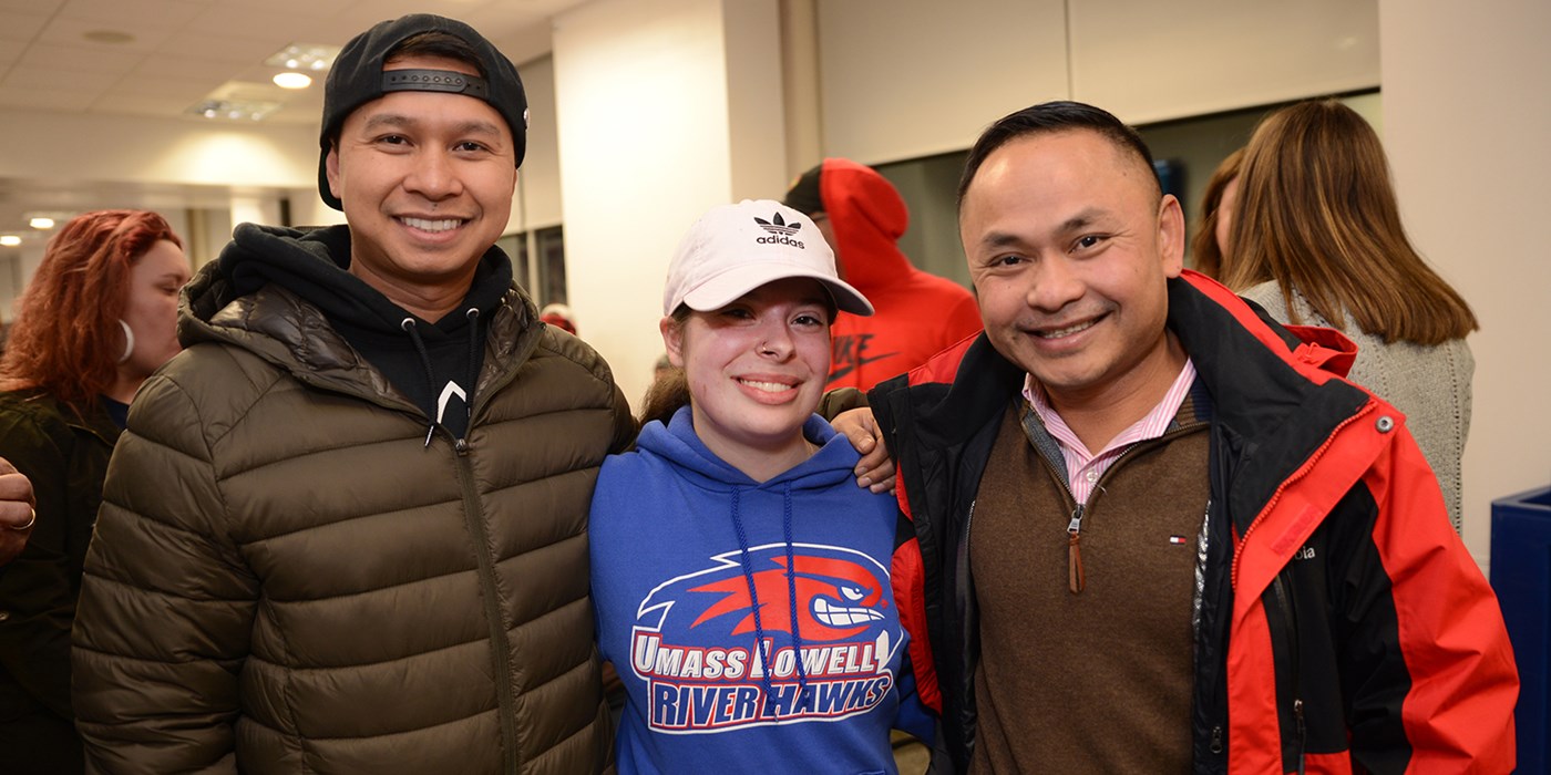 Family of Asian decent poses for a photo, two men and woman wearing UMass Lowell branded sweatshirt at Acre Hockey Night, Friday, February 2, 2019 at the Tsongas Center
