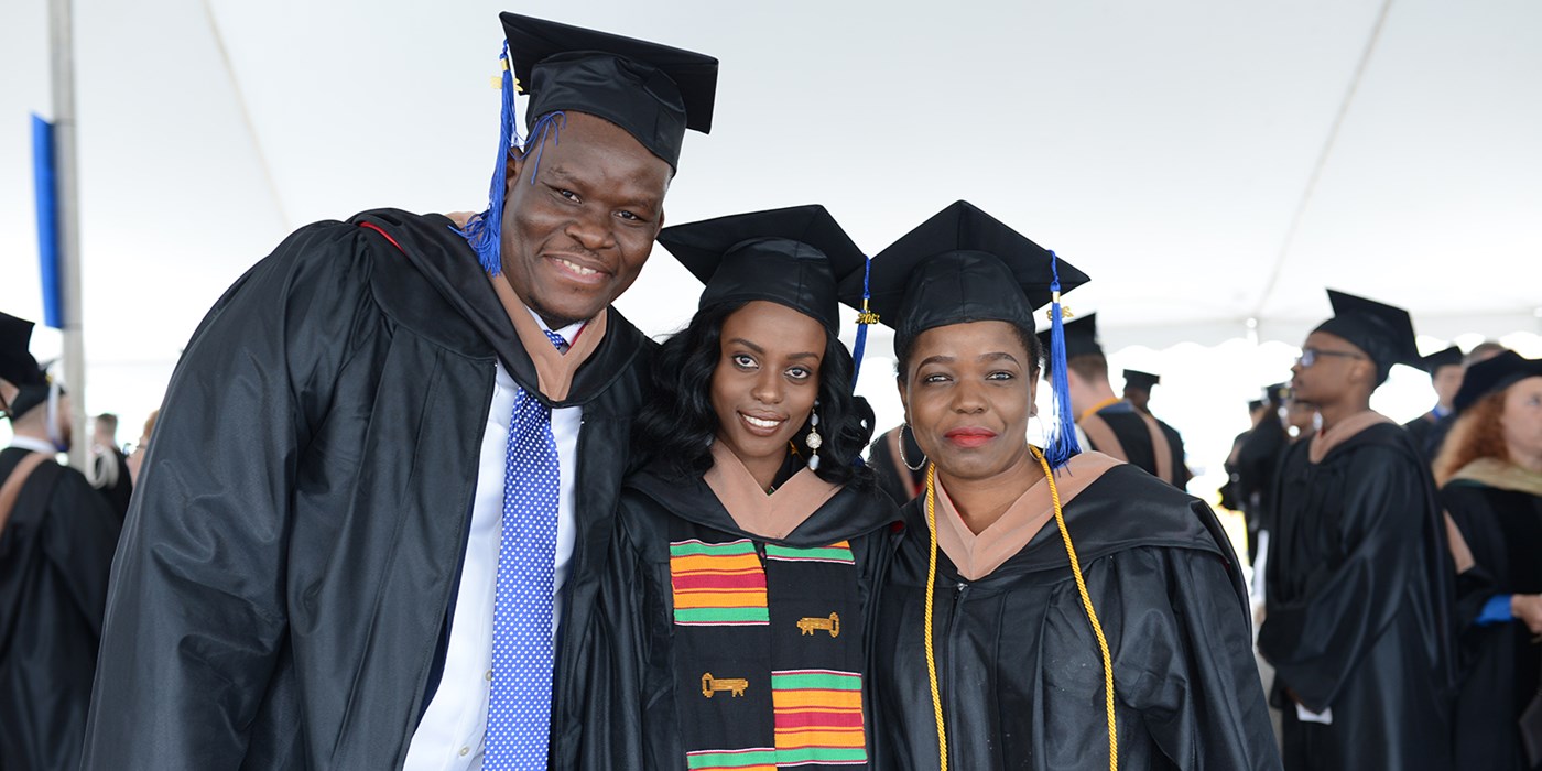 Family? posing for photo at 2018 Commencement ceremonies: Left-to-right: African American male, and two African American females all in cap and gowns posing.  