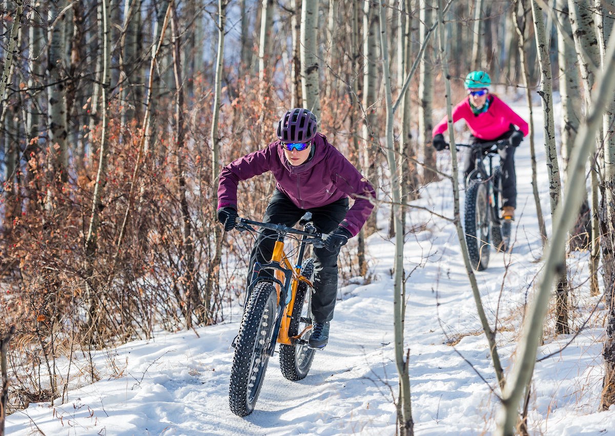 Two people travel on bikes with fat tires on a snowy path in the woods