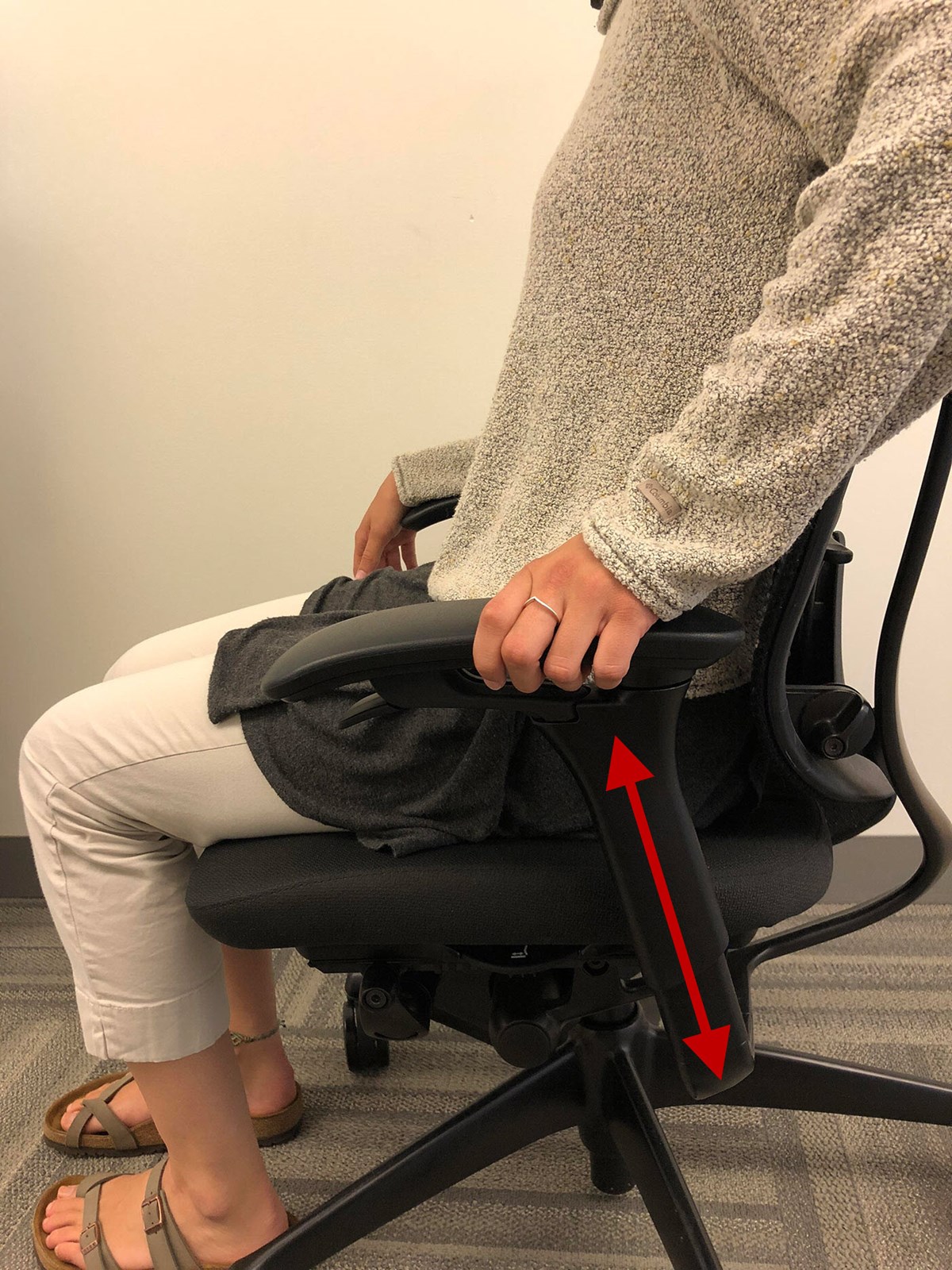 A female sitting in a contessa chair pulling or pushing on the armrest showing that the armrest can be adjusted up or down.