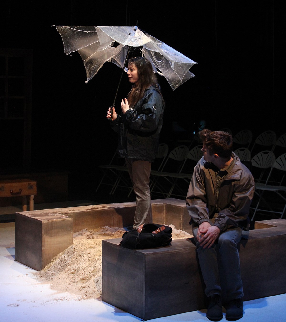 A female holding an umbrella on stage while a male student looks on during a UMass Lowell Theatre Arts production.