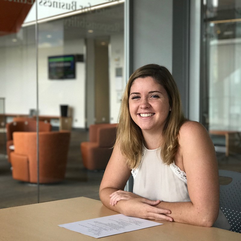 A smiling female student sitting at a table inside the Pulichino Tong Business Building at UMass Lowell. The Pulichino Tong Building will be at the heart of the North Campus Innovation District, which brings the university’s engineering, science and business programs together for students, entrepreneurs and industry partners.