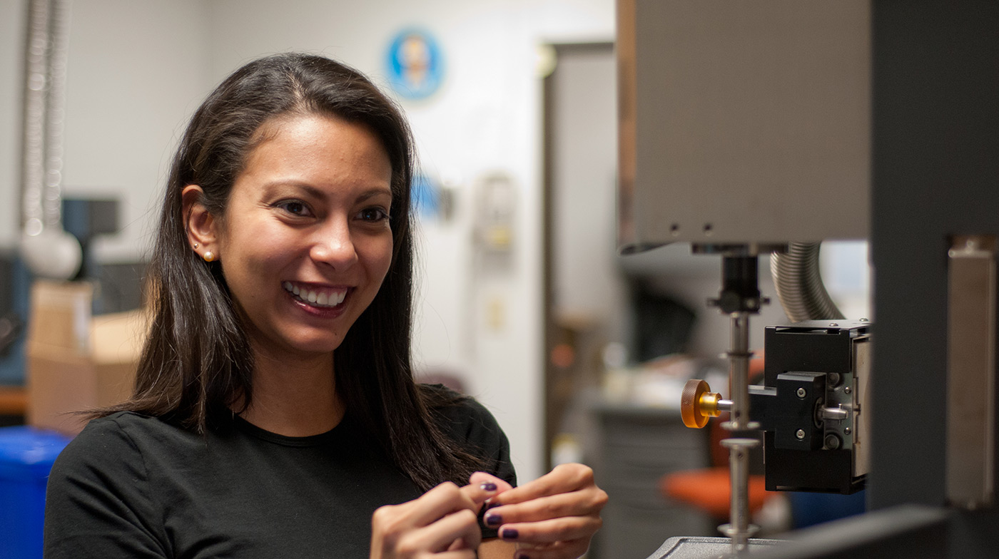 A female UMass Lowell student working in a Plastics Engineering lab and smiling.