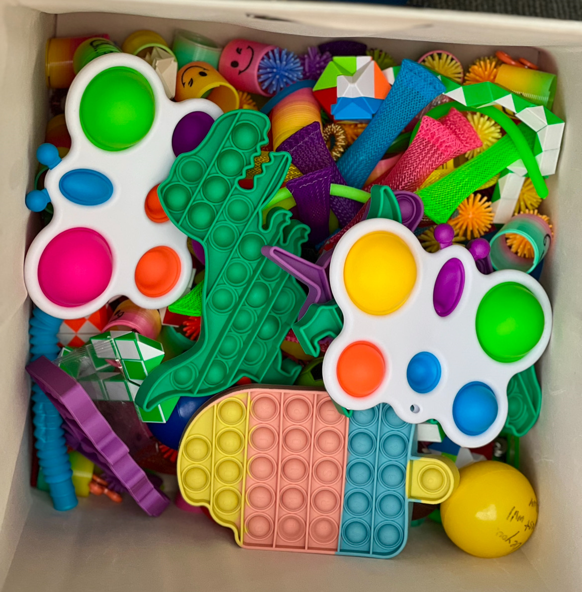 An array of colorful fidget toys including dinosaur and ice cream cone pop-its, slinkys, butterfly poppers, and more.