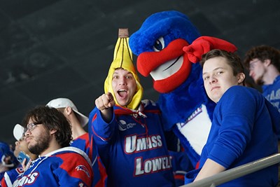 A student in a banana costume points at the camera while standing next to a River Hawk mascot at a hockey game