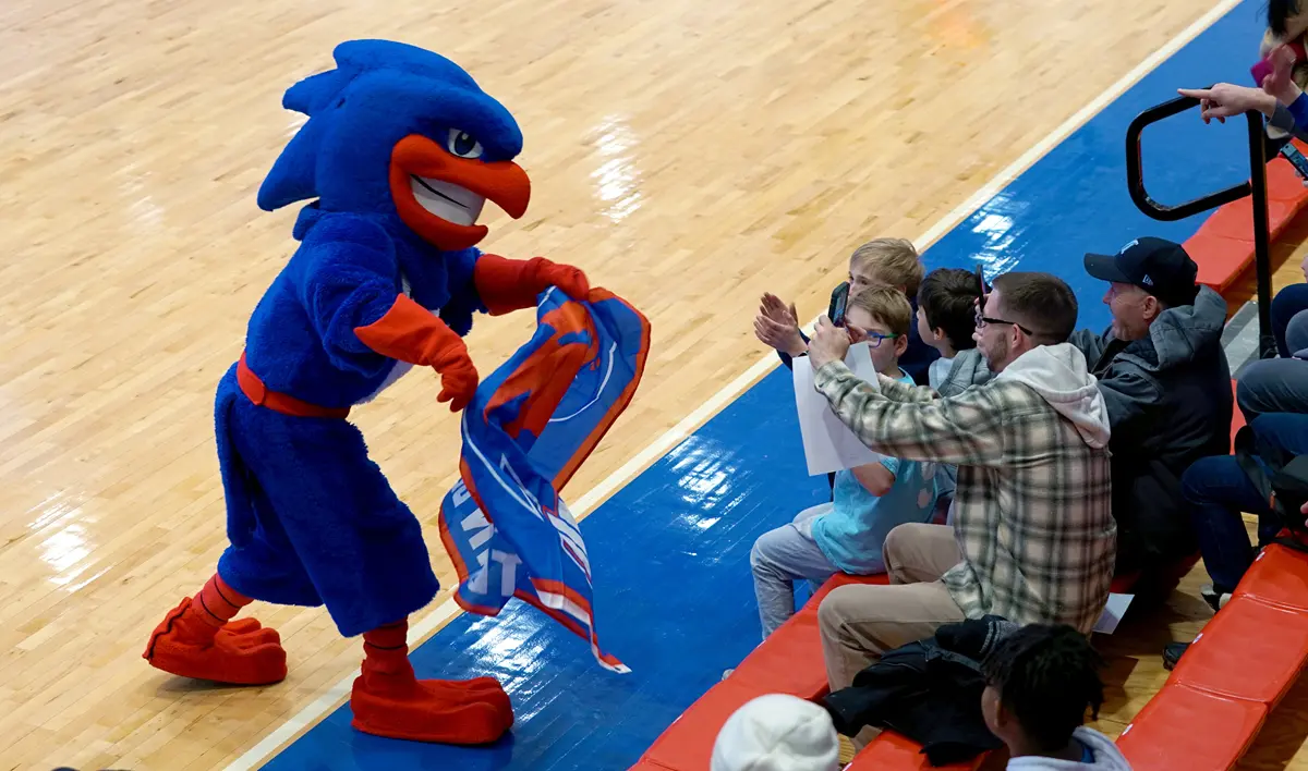 Garrett Kelly as UMass Lowell mascot, Rowdy the River Hawk, waves a flag and interacts with the courtside crowd.