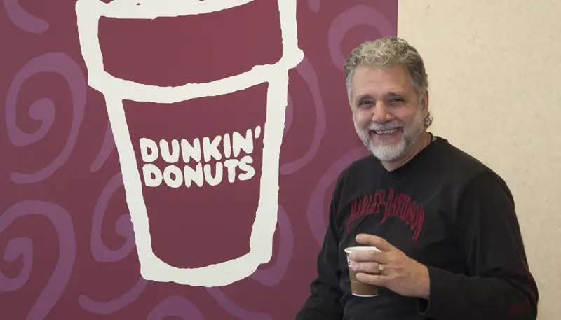 George Zografos holds a cup of coffee in one of his former Dunkin' Donuts locations on Cape Cod