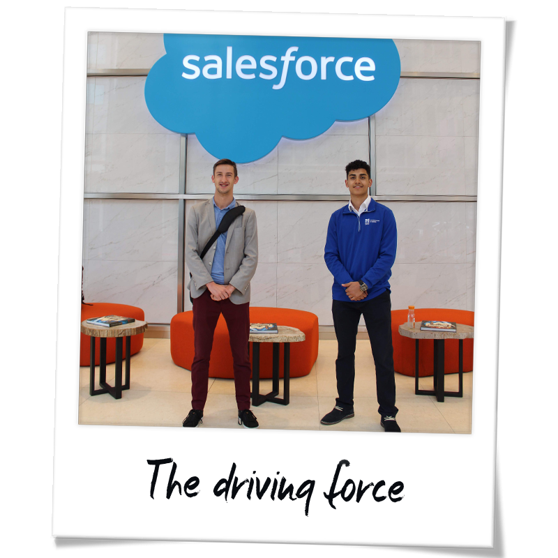 "Polaroid" photo of Gianni Newman (right) and another Manning School of Business student in front of a Salesforce sign in Salesforce Tower in San Francisco - handwriting on the frame reads "The driving force"
