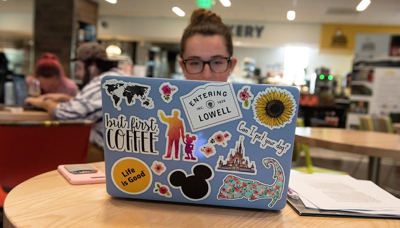 UMass Lowell student works in the library on a laptop covered in colorful stickers