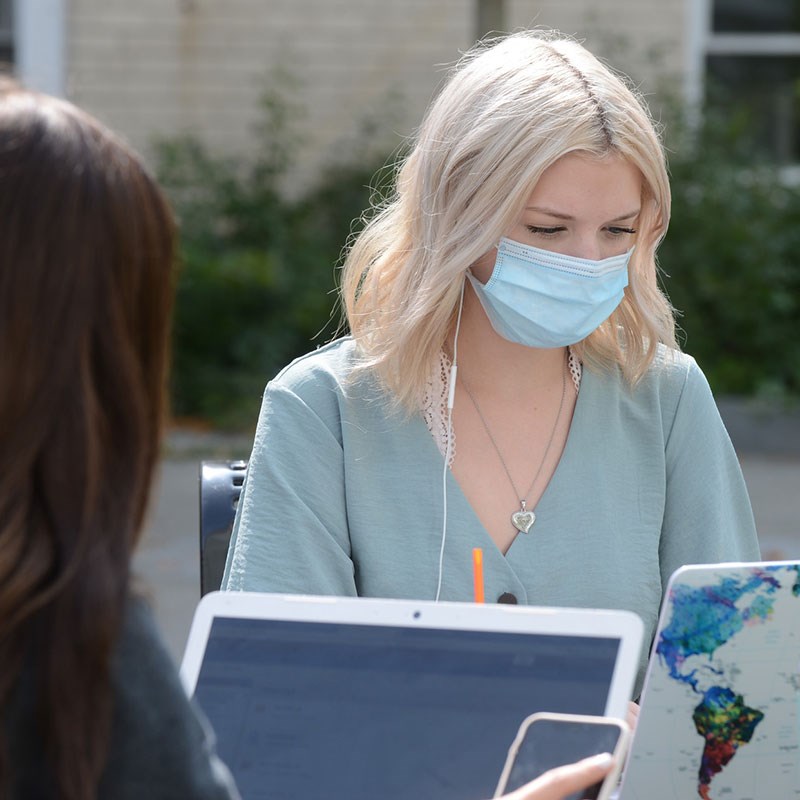 Young woman wearing mask works on laptop outdoors