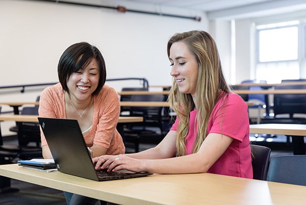 Two graduate students work together on laptop in classroom.