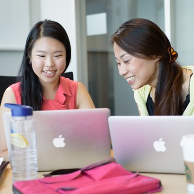 Two female grad students work on their laptops