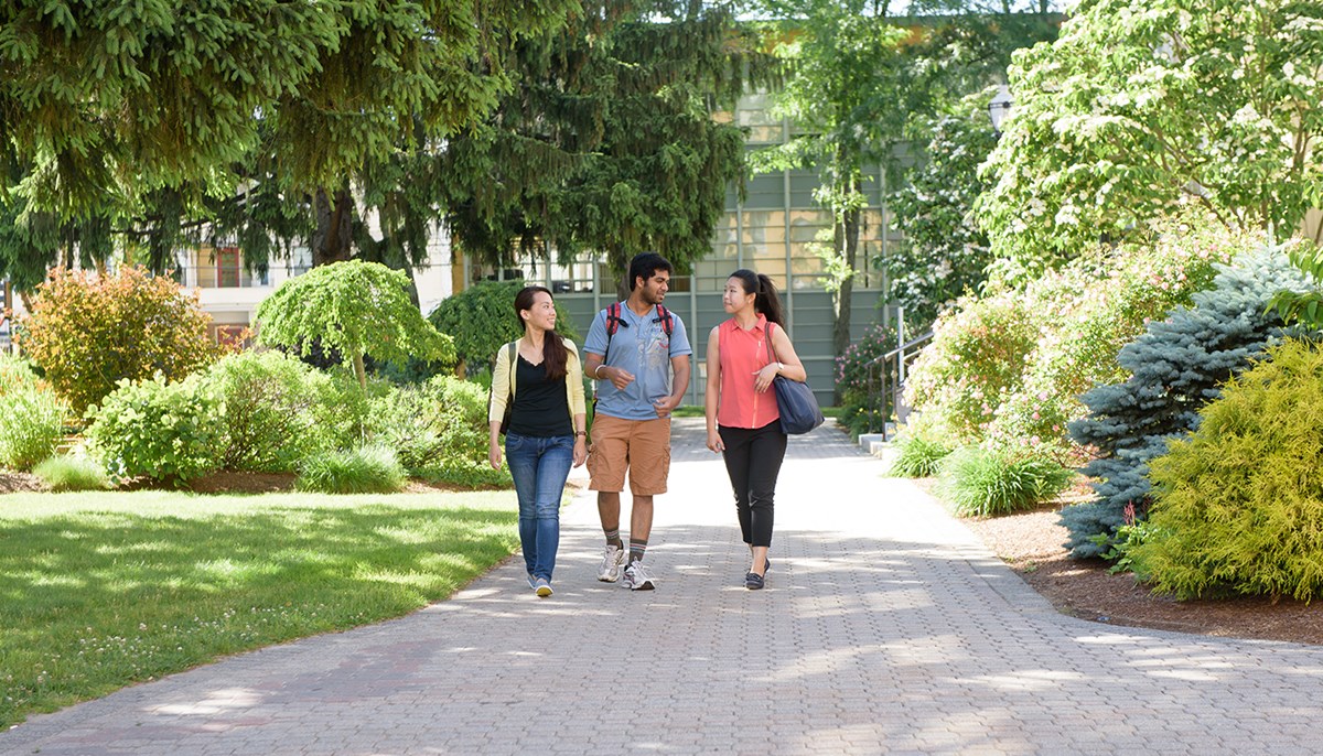 Three graduate students walking outside on North Campus surrounded by greenery in the summer at UMass Lowell