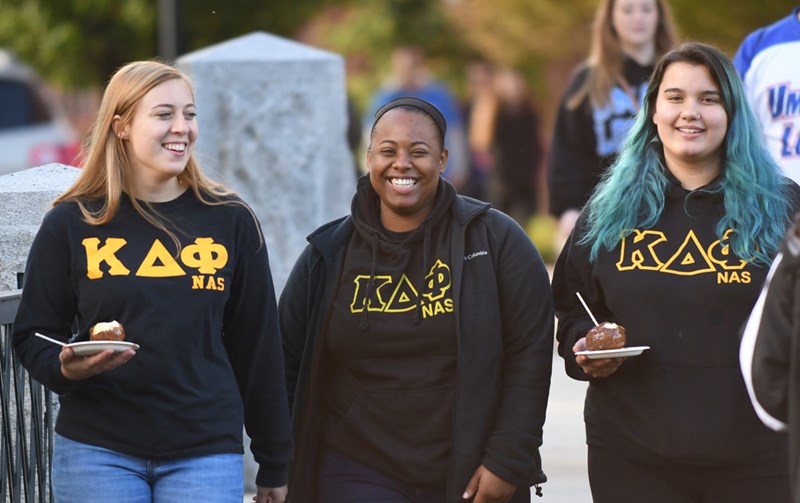 Three female students at the homecoming festival smiling wearing matching Kappa Delta Phi sweatshirts