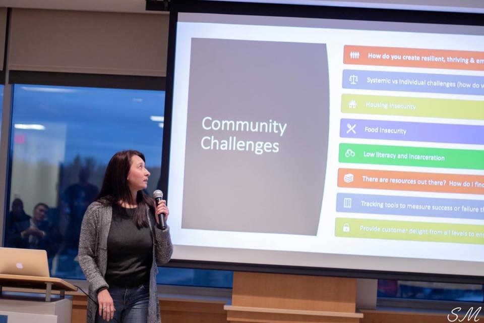Person with microphone in front of screen with "Community Challenges".