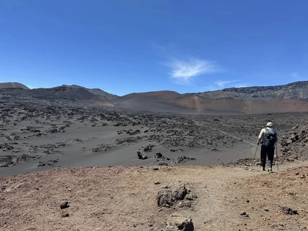 One man walks towards a lunar landscape valley under a blue sky.