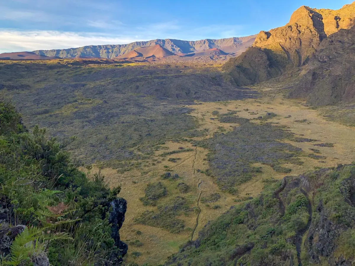 A flat valley lies below a high viewpoint with volcanic craters and blue sky in the background.