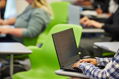 Student types on a laptop in a classroom